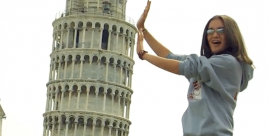 Perillo Tours Why Perillo video thumbnail shows a young female tourist on a Perillo Tour of Italy is pretending to hold up the Leaning Tower of Pisa (video production by Merging Media).