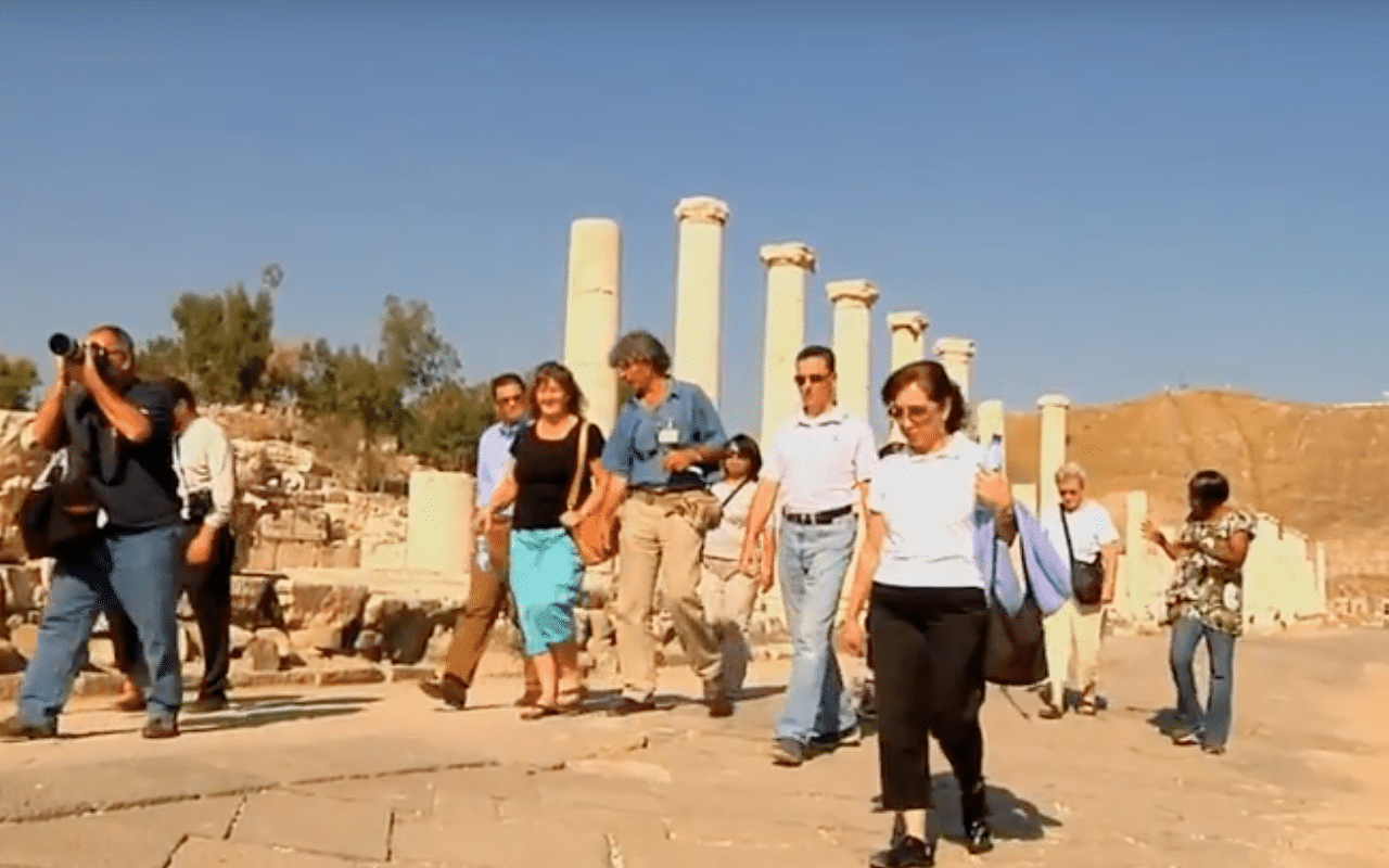 Perillo Tours Discover Israel commercial thumbnail features a group of Perillo Tours tourists walking along stone pillars that belong to the site of the once thriving ancient ruins of Israel (video production by Merging Media).