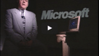 USWeb IE 4 Deployment video thumbnail is of an older gentleman wearing a gray suit with a black and gray tie, stands next to a 1990's style laptop set on an ionic style short pillar, word in background reads, Microsoft.