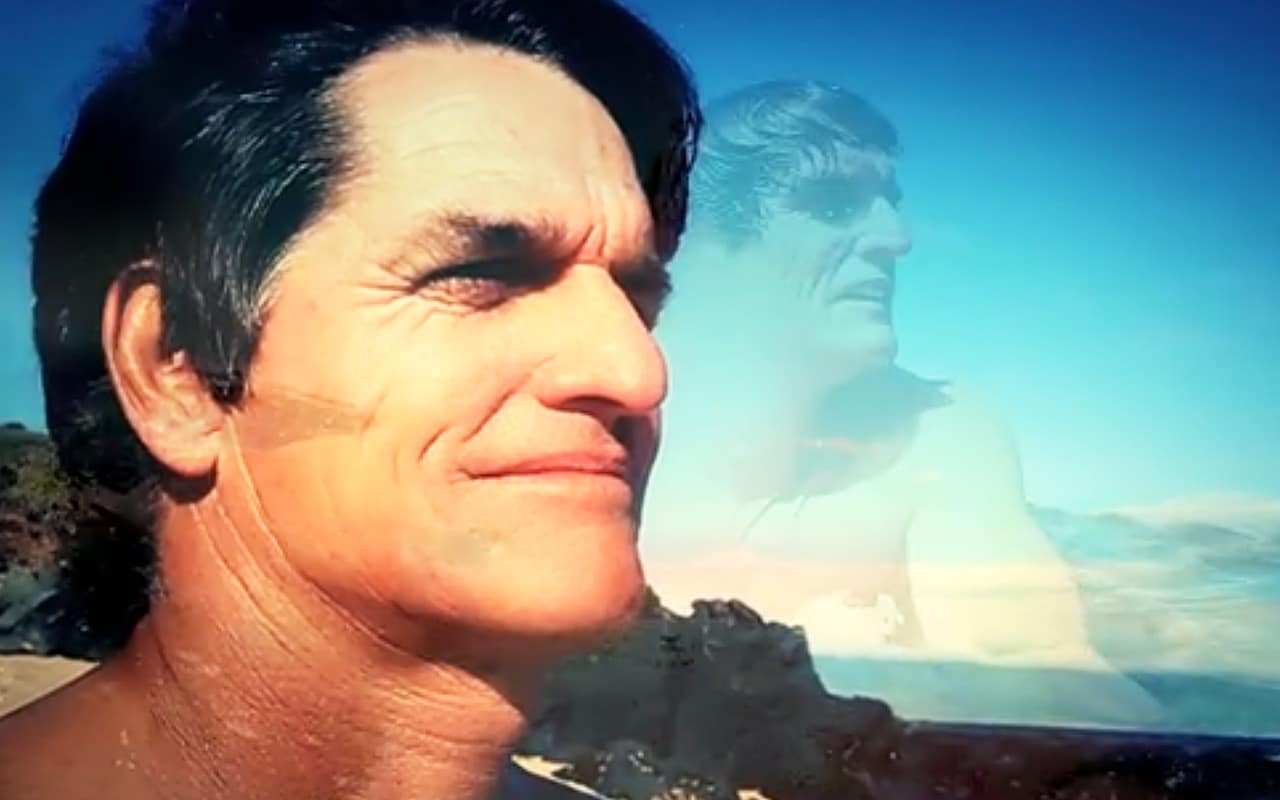 Close up of middle aged man (Buzzy Kerbox) from the neck up in foreground, with transparent image of the same man on a surfboard is behind him during an interview for Bobrick Mana conference (video produced by Merging Media).